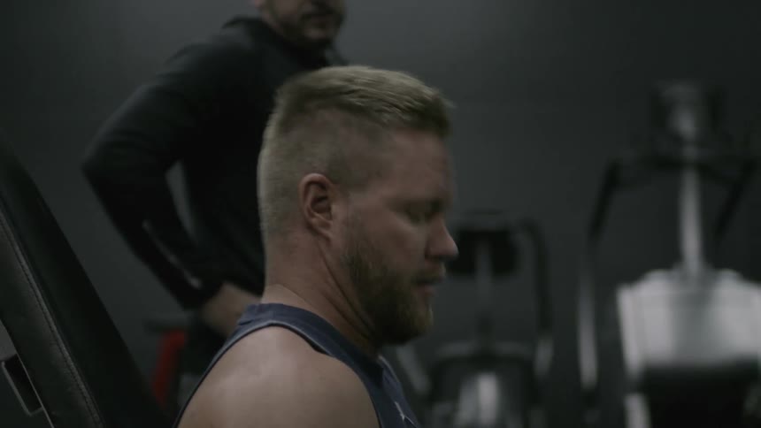 A man is lifting weights and talking with someone in a gym