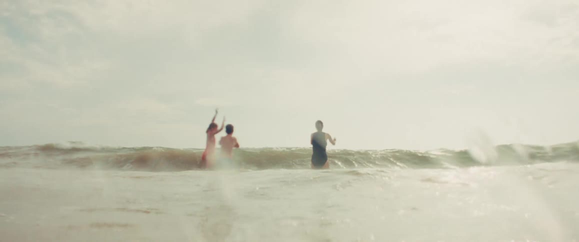 A mother and her two children jump and play in the ocean waves in a beautiful slow-motion shot from the water's perspective