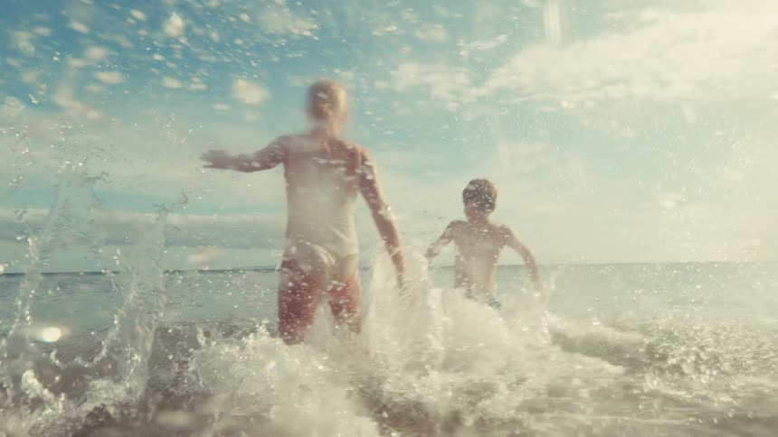 Carefree children joyfully run and splash into the ocean waves in cinematic slow motion