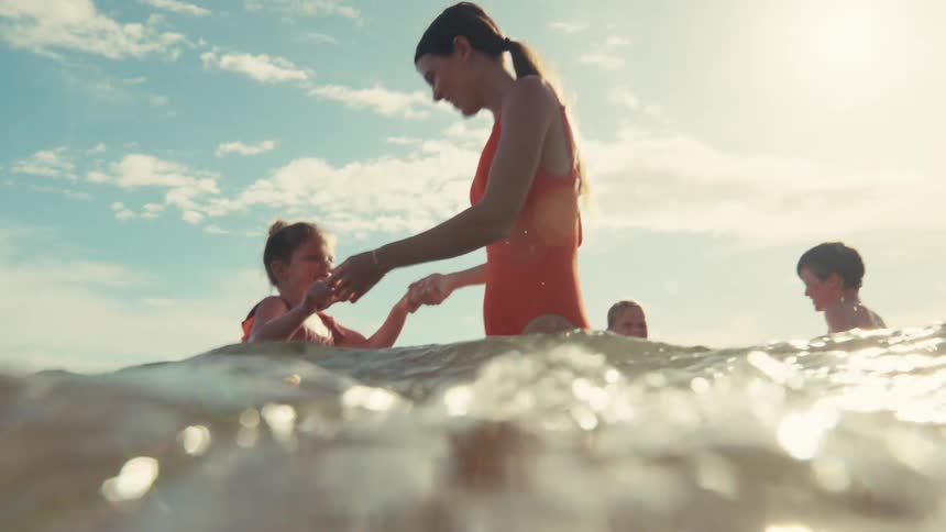 A happy mother in a red swimsuit enjoys a sunny day at the beach, playing in the shimmering ocean water with her children