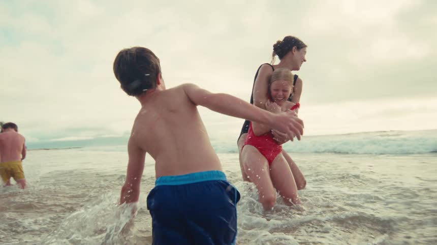 A joyful family splashes and plays together in the ocean waves during a beach vacation in slow motion