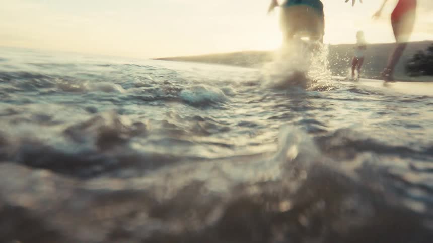 Slow motion shot of a young boy running and splashing in the shallow ocean water along the beach during a beautiful sunset