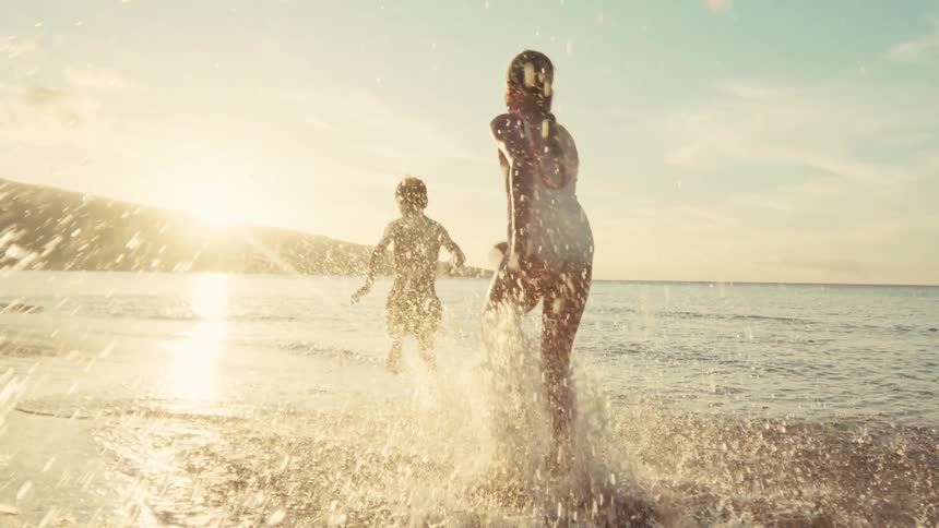 Two children run and splash through the shallow ocean water at sunset in a beautiful slow motion cinematic shot