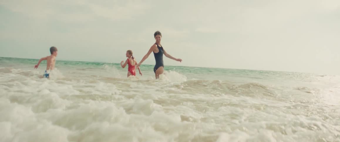 Slow motion shot of a mother and her children running and joyfully jumping into the ocean waves