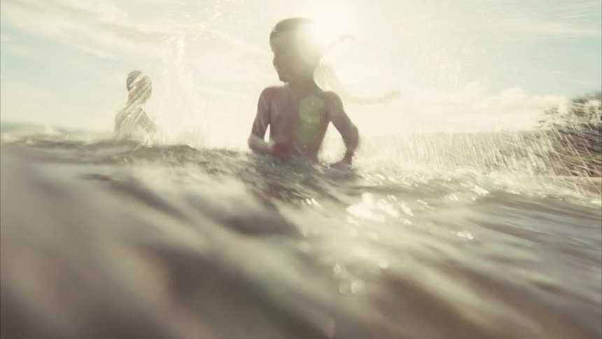 Dreamy slow-motion footage captures joyful kids splashing water at the camera while playing in the ocean on a sunny day