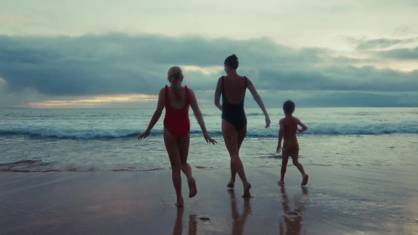 A happy family with a young boy and girl run towards the ocean in slow motion during a beautiful sunset