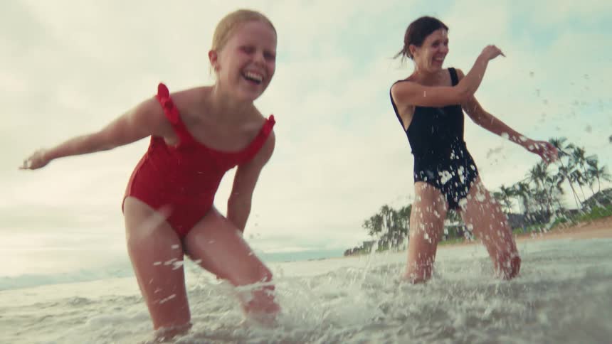 A joyful mother and her children laugh as they splash each other in the shallow ocean waves in slow motion