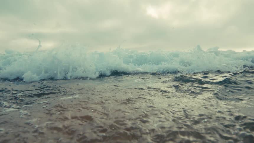 A dramatic slow-motion shot from the water's surface as a powerful ocean wave crests and crashes towards the camera