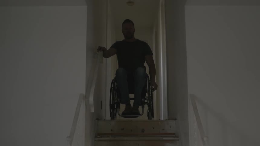 Man in wheelchair roll up and stops at stairs in hallway