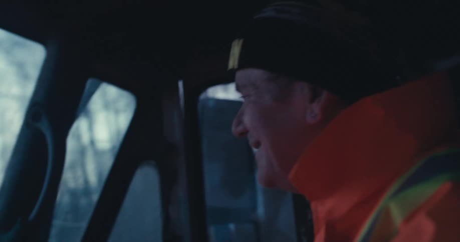 Close-up of a happy male truck driver in a high-visibility jacket smiling as he drives his rig from the pre-dawn darkness into the morning light