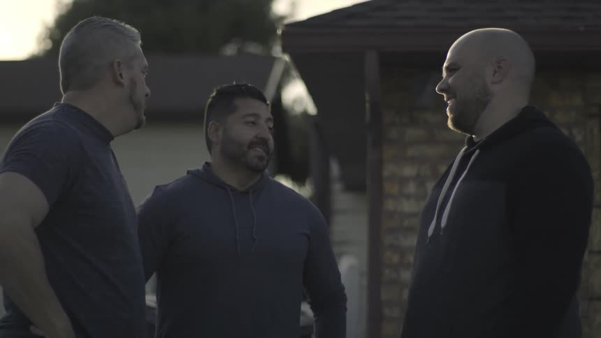 Men talk and laugh while standing outside a house
