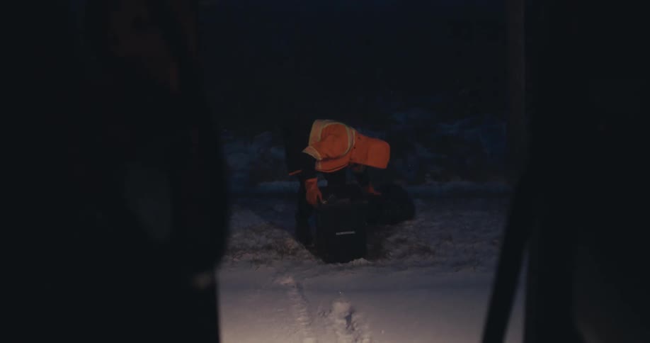 View from inside a truck of a sanitation worker collecting garbage in the snow on a cold night