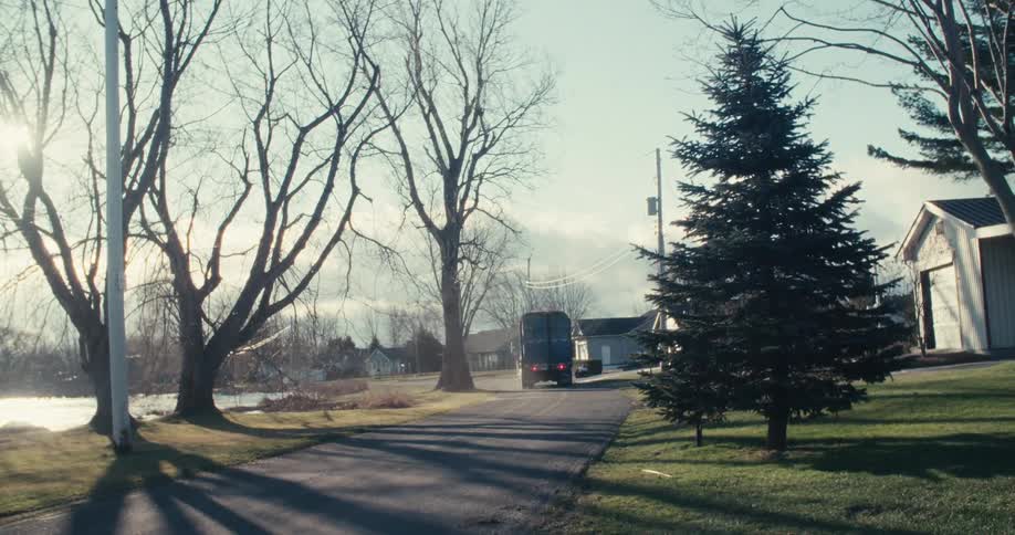 A garbage truck drives down a quiet, sunny suburban street next to a river