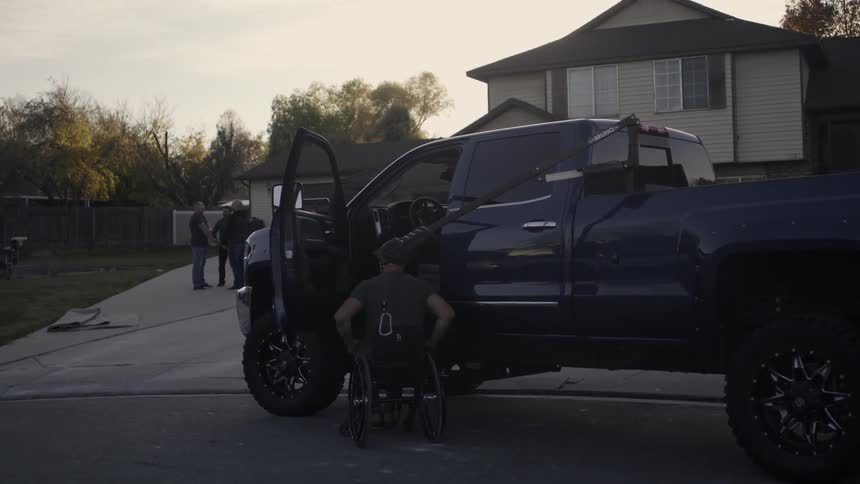 A man exits a pickup truck and gets in a wheelchair