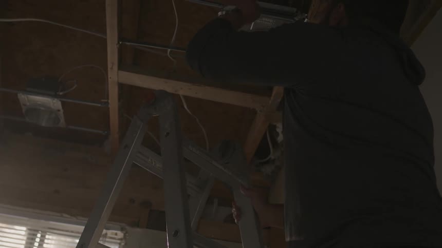 Man climbs up a ladder in  a garage on a sunny day