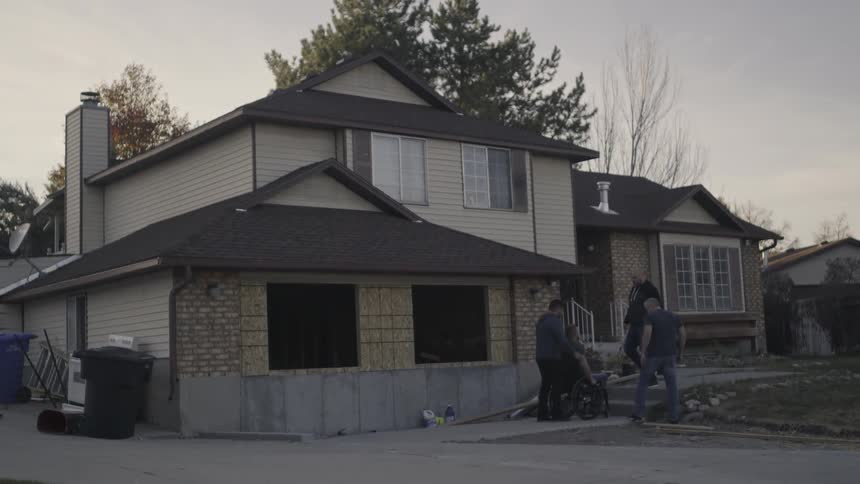 People carry a man in a wheelchair up some steps outside