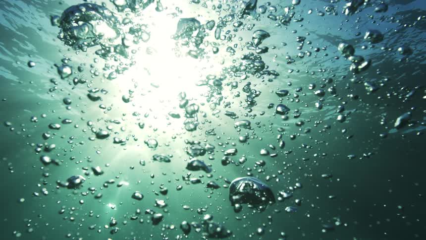 Mesmerizing slow-motion shot from underwater captures air bubbles rising to the sunlit surface