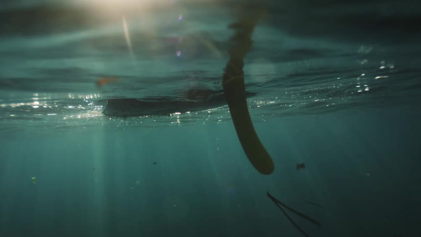 An artistic underwater view of a surfboard floating peacefully as beautiful sun rays shine through the water's surface