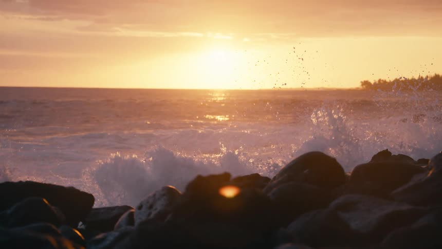 Majestic ocean waves crash in slow motion against a rocky shoreline during a brilliant golden sunset