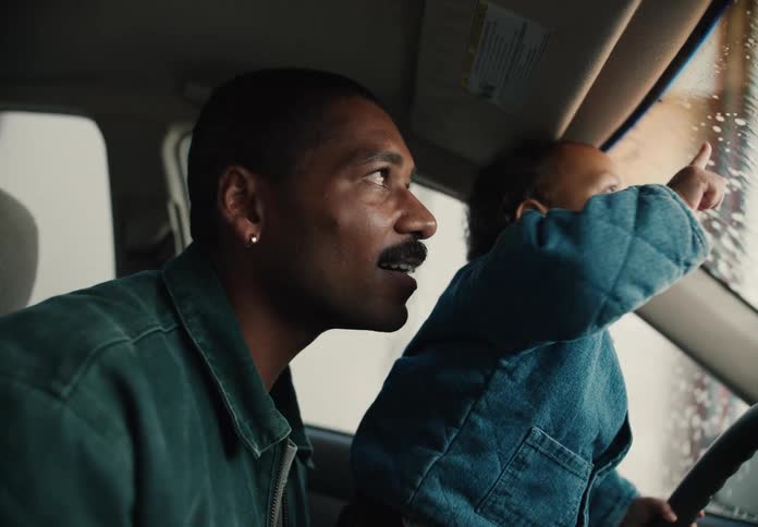 An excited toddler on his father's lap points at the window as they go through a car wash