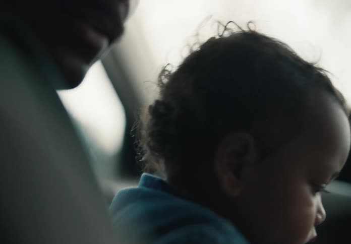 A close-up of a curious baby with curly hair sitting in the driver's seat of a car, reaching for the steering wheel