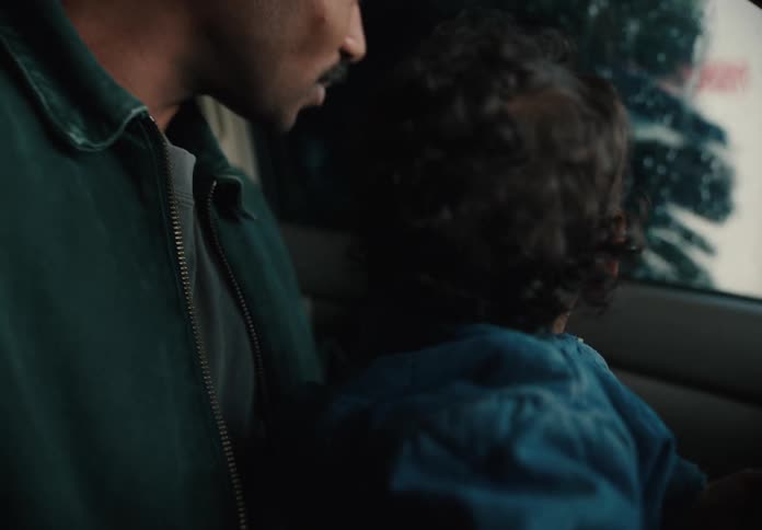 A loving father holds his toddler on his lap as they watch the spinning brushes and water of an automatic car wash with wonder