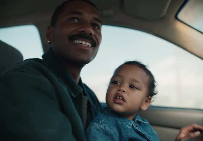 An African American father and his toddler son share a tender moment while driving in a car, the child sitting on his lap and watching the road