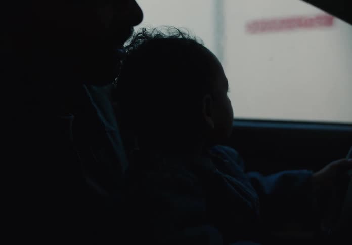 An adorable baby claps with excitement while sitting on its father's lap as they drive through a car wash