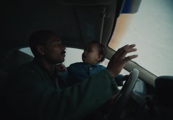 A loving father shares a tender moment with his toddler in the car, letting the child hold the steering wheel on a rainy day