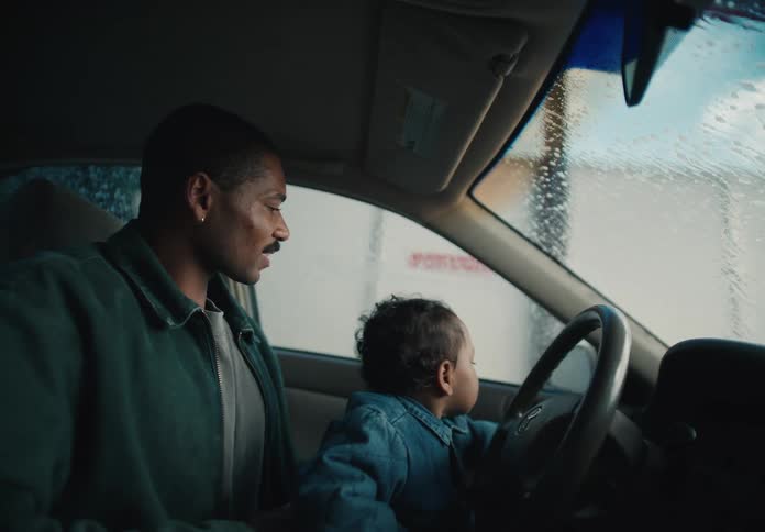 A Black father and his toddler son share a moment of wonder and excitement while going through an automatic car wash