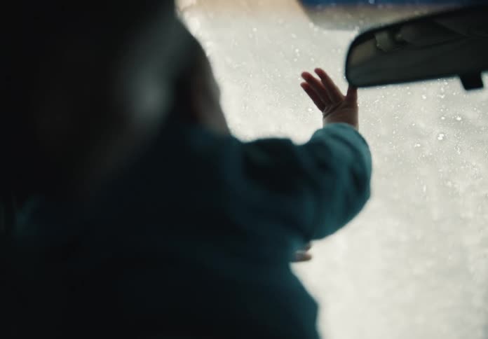 A person's hands move in a slow dance against the soapy window of a car going through a car wash