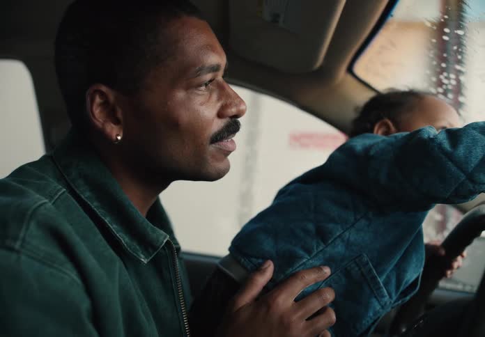 A loving father holds his toddler son on his lap while the child pretends to drive their car through an exciting car wash