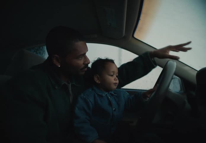 Father sits with toddler in the driver’s seat, pointing through the windshield during a quiet car wash moment