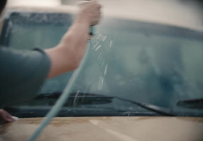 A young man hoses down his tan truck in a close-up slow motion shot