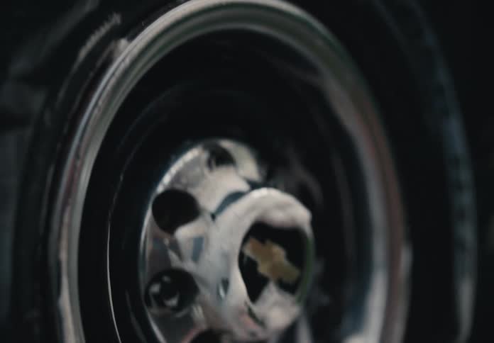 A close-up of a person's hand washing the chrome hubcap and rim of a car wheel with a soapy sponge