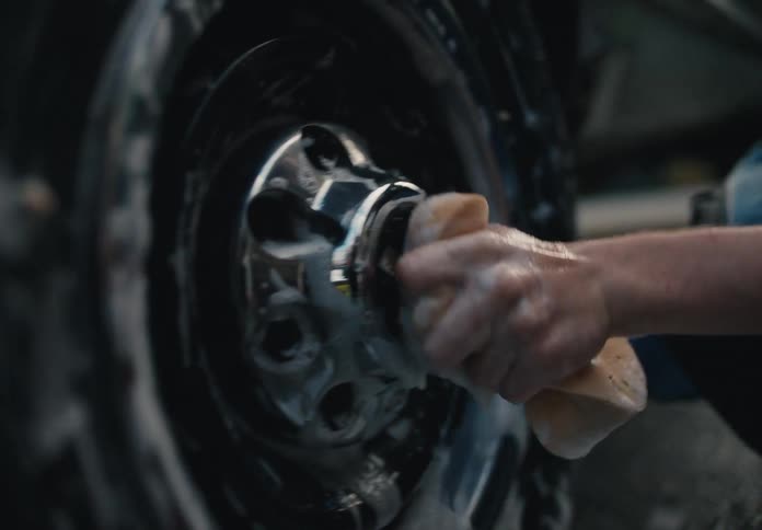 A young man meticulously washes the soapy wheel of a car with a sponge in slow motion