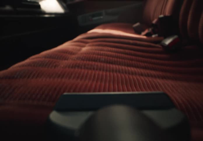 A close-up, point-of-view shot of a vacuum cleaner cleaning the red fabric seat of a vintage car