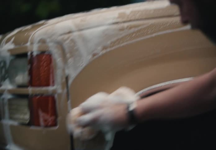 Close-up slow-motion detail of a man washing a vintage tan truck with a soapy sponge