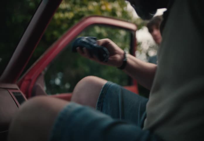 A bearded man gets into his vintage red pickup truck while holding a blue bandana