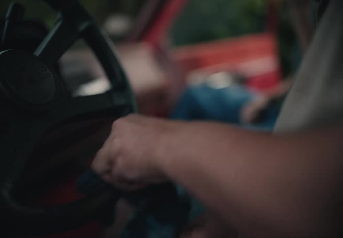 A bearded man carefully cleans the steering wheel of his vintage red pickup truck with a blue cloth