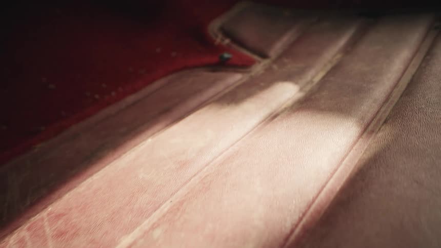 A slow pull-back shot reveals the dusty and worn red interior floor of an abandoned classic car