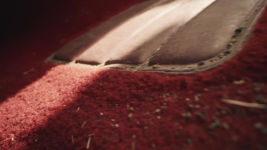 An extreme close-up slow pan reveals dirt and debris on a red carpeted floor