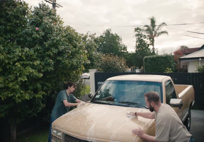A father and his teenage son bond while washing their pickup truck together in the driveway on an overcast day