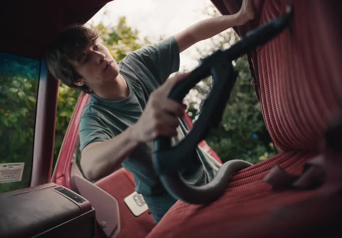 Teenage boy carefully vacuums the seats and floor of his vintage red truck parked in the driveway