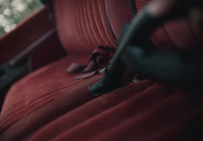 A person vacuums the dirty red fabric seats of a vintage car in slow motion
