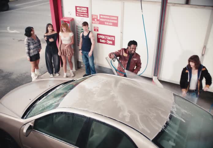 A diverse group of young friends wash a sedan together at a self-service car wash bay