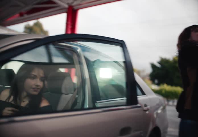 A stylish young woman confidently gets out of her car in slow motion at an outdoor car wash