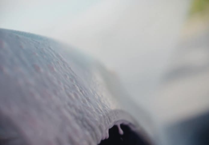 A close-up, slow-motion shot of pink car wash foam slowly dripping down the fender of a car