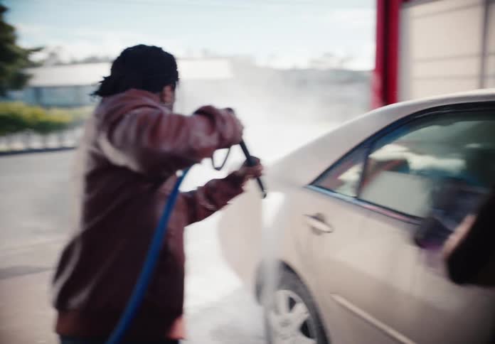 A group of diverse friends have fun washing their car together at a self-service car wash in slow motion