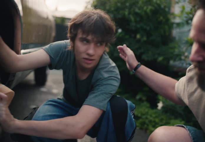 A caring father affectionately pats his teenage son on the back while they wash a car together in their driveway